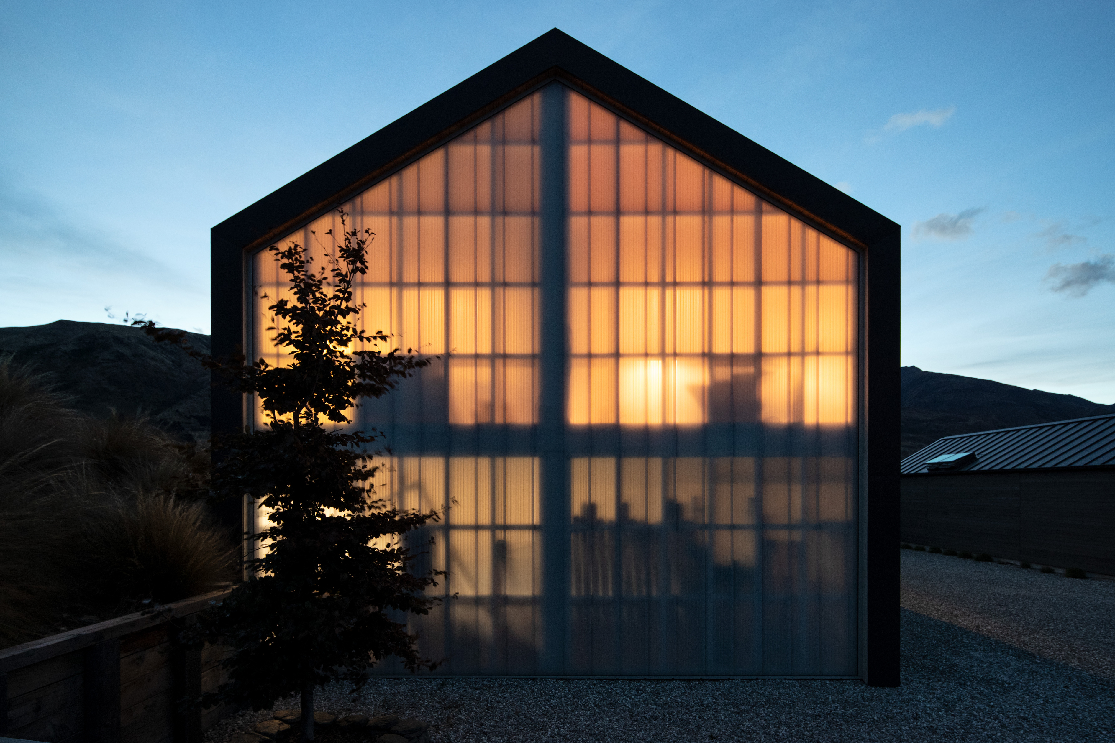 Exterior of Wanaka barn-style loft at night, with light shining through floor-to-sealing translucent polycarbonate